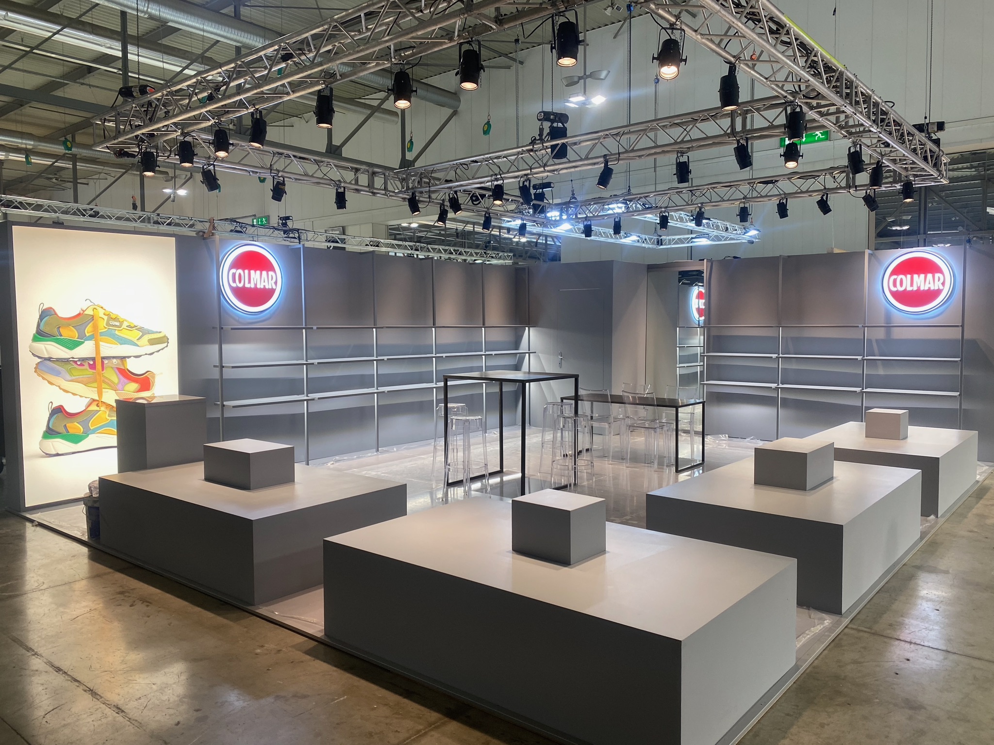 Stand Colmar montato a MICAM prima dell'apertura, con pareti espositive, pedane per i prodotti e illuminazione sospesa.