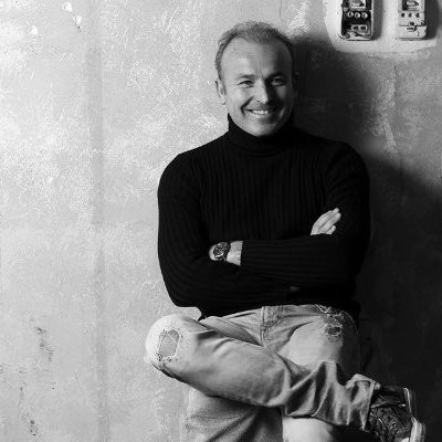 Nicola Sarti seduto con le braccia conserte, in un ritratto in bianco e nero.