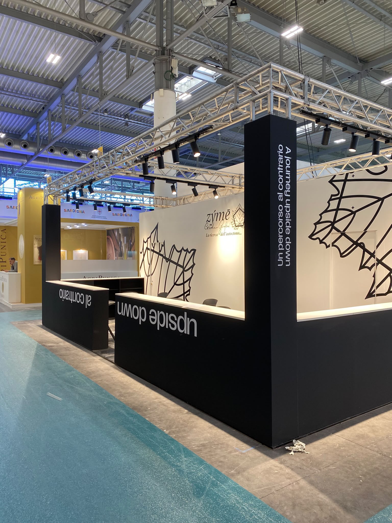 Vista d'angolo dello stand Zýmē a Vinitaly 2026, con pareti grafiche e volumi neri.